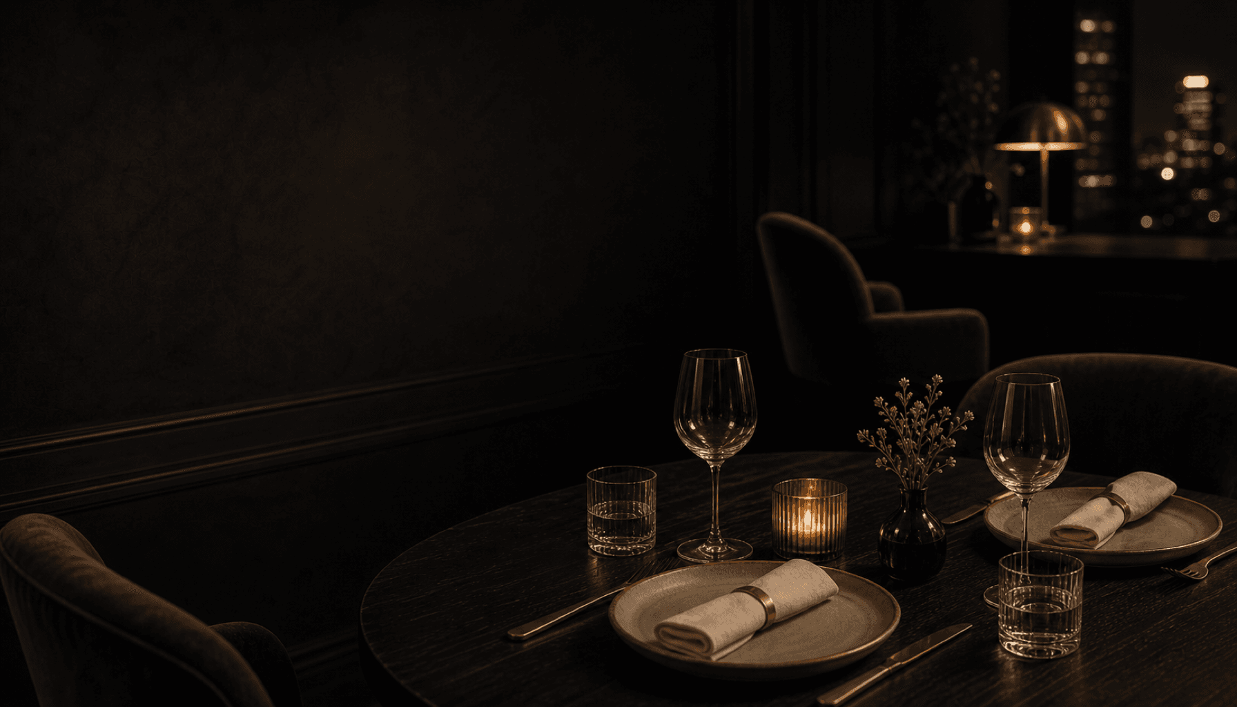 A candlelit dinner table set for two in a quiet charcoal room.